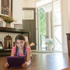 A girl is laying on the floor using her tablet.