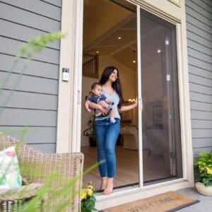 A woman holding her baby in front of a screen door.